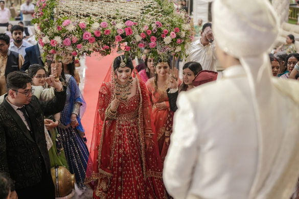 Bride entering wedding venue under floral chadar held by family