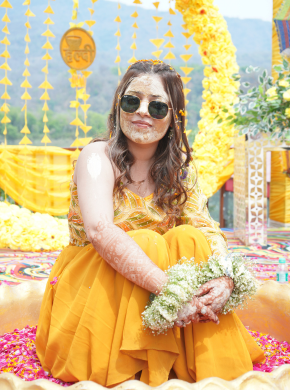 Woman posing in bright yellow attire at haldi ceremony with decor